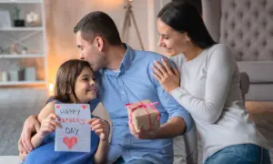 Córka wręcza tacie kartkę z napisem "Happy Father's Day" i prezent. Mama obejmuje męża. Piękny wiersz dla męża czeka na odczytanie.
