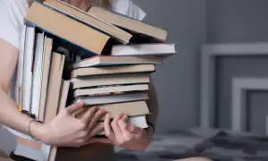 Osoba trzyma stos książek, zastanawiając się, gdzie oddać używane książki.