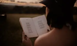 Kobieta w czapce czyta książkę z pięknymi wierszami dla niej, w otoczeniu natury o zachodzie słońca.