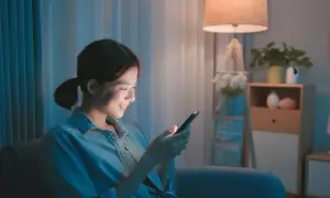 Uśmiechnięta dziewczyna pisze wiersze na dobranoc dla chłopaka na telefonie, siedząc wieczorem w przytulnym pokoju.