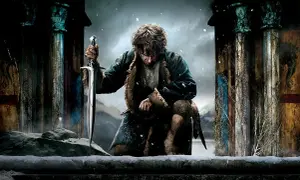 Bilbo Baggins, jak wygląda hobbit, klęczy w śniegu, trzymając miecz. W tle ruiny i zimowy krajobraz.