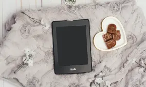 Elegancki Kindle na miękkim kocu z różami, obok serduszka z czekoladkami. Idealny zestaw, by dowiedzieć się, jak pobierać książki na Kindle.