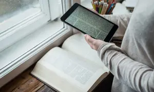 Osoba porównuje tekst na tablecie z otwartą księgą. Czy warto czytać książki? Przykłady z literatury inspirują do poszukiwań.