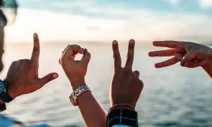 Dłonie tworzą napis LOVE. Idealny wierszyk dla zakochanych, gdy słońce zachodzi nad wodą.