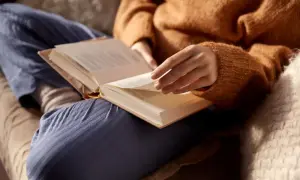Osoba w swetrze czyta książkę, szukając argumentów, czy warto czytać książki. Ciepły, przytulny kadr.
