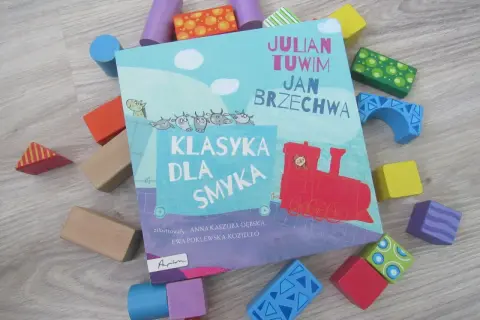 Książka "Klasyka dla smyka" z wierszami Tuwima i Brzechwy, otoczona kolorowymi klockami. Czytanie jej to jak zabawa, a nie jak szukanie karaluchów pod poduchy.