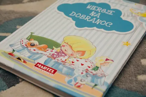 Książka "Wiersze na dobranoc" z dziewczynką śpiącą z misiem i zabawkami.