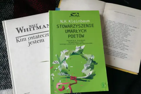 Zielona okładka "Stowarzyszenia Umarłych Poetów" N.H. Kleinbauma. Obok biała książka Walta Whitmana.