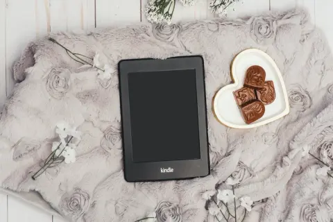 Elegancki Kindle na miękkim kocu z różami, obok serduszka z czekoladkami. Idealny zestaw, by dowiedzieć się, jak pobierać książki na Kindle.