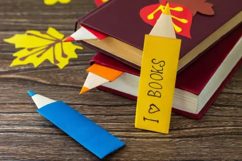 Jak zrobić ładną zakładkę do książki w kształcie kredki. Kolorowe zakładki wsuwają się między strony, a jedna z nich ma napis "I ♡ BOOKS".