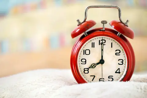 Czerwony budzik na białym tle, pokazuje 8:00. Czas na wierszyk na dzień dobry dla niego!
