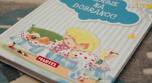 Książka "Wiersze na dobranoc" z dziewczynką śpiącą z misiem i zabawkami.