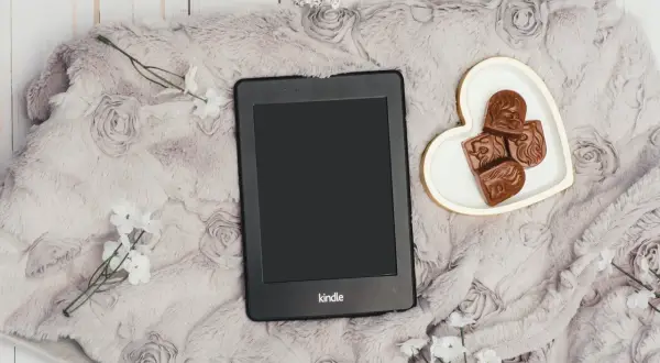 Elegancki Kindle na miękkim kocu z różami, obok serduszka z czekoladkami. Idealny zestaw, by dowiedzieć się, jak pobierać książki na Kindle.