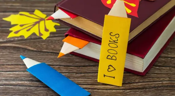 Jak zrobić ładną zakładkę do książki w kształcie kredki. Kolorowe zakładki wsuwają się między strony, a jedna z nich ma napis "I ♡ BOOKS".