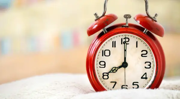 Czerwony budzik na białym tle, pokazuje 8:00. Czas na wierszyk na dzień dobry dla niego!