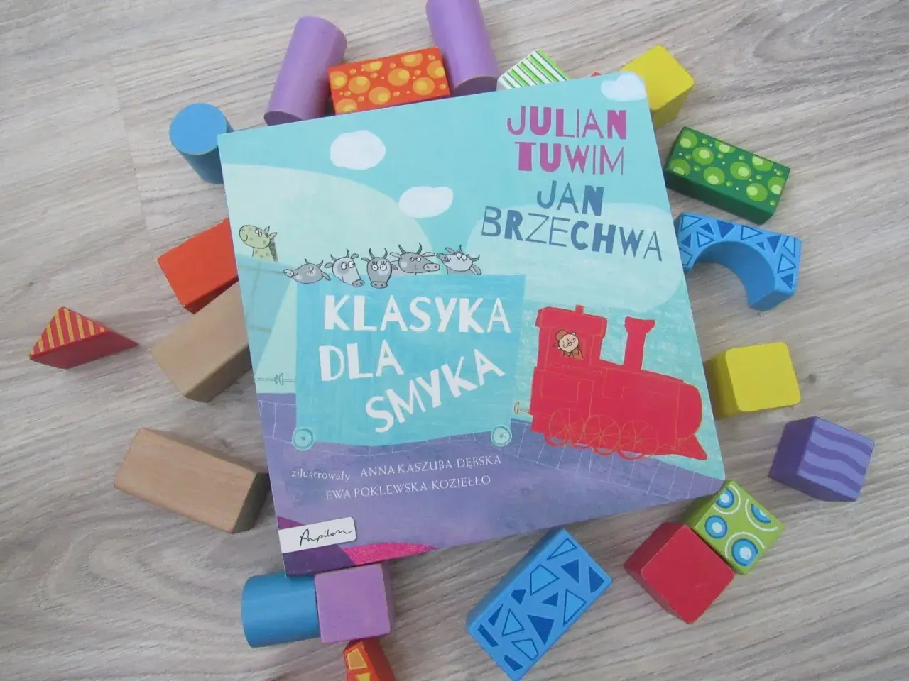 Książka "Klasyka dla smyka" z wierszami Tuwima i Brzechwy, otoczona kolorowymi klockami. Czytanie jej to jak zabawa, a nie jak szukanie karaluchów pod poduchy.