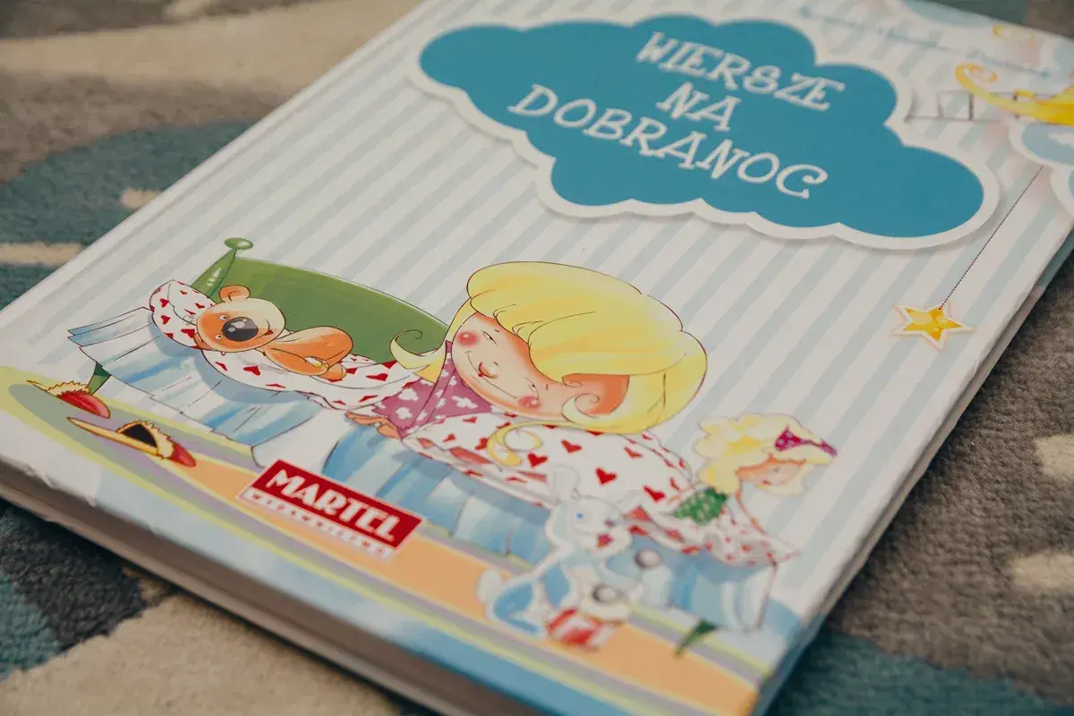 Książka "Wiersze na dobranoc" z dziewczynką śpiącą z misiem i zabawkami.