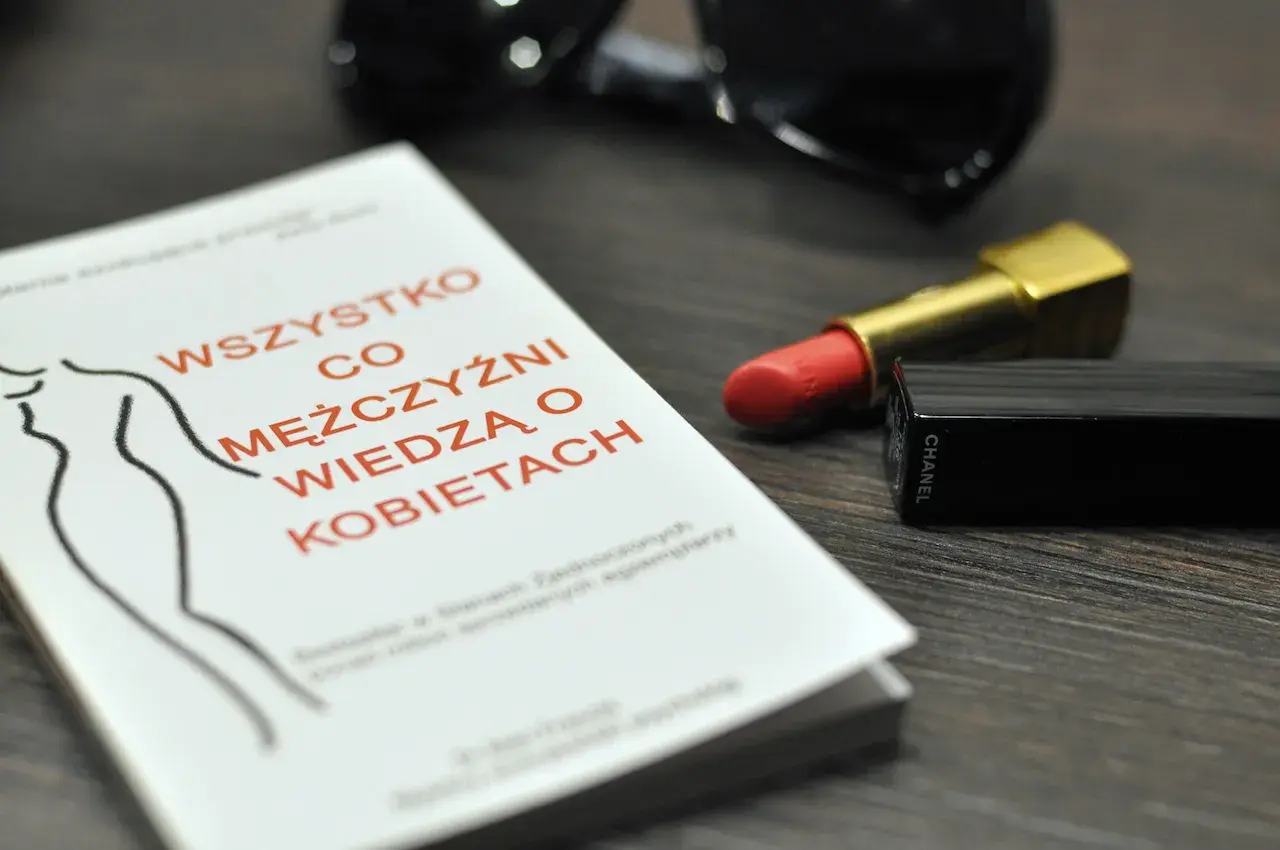 Książka "Wszystko co mężczyźni wiedzą o kobietach", szminka Chanel i okulary przeciwsłoneczne.