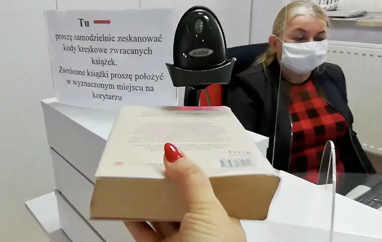 Instrukcja jak oddać książki do biblioteki: zeskanuj kod kreskowy i połóż książkę w wyznaczonym miejscu. Bibliotekarka w maseczce czeka.