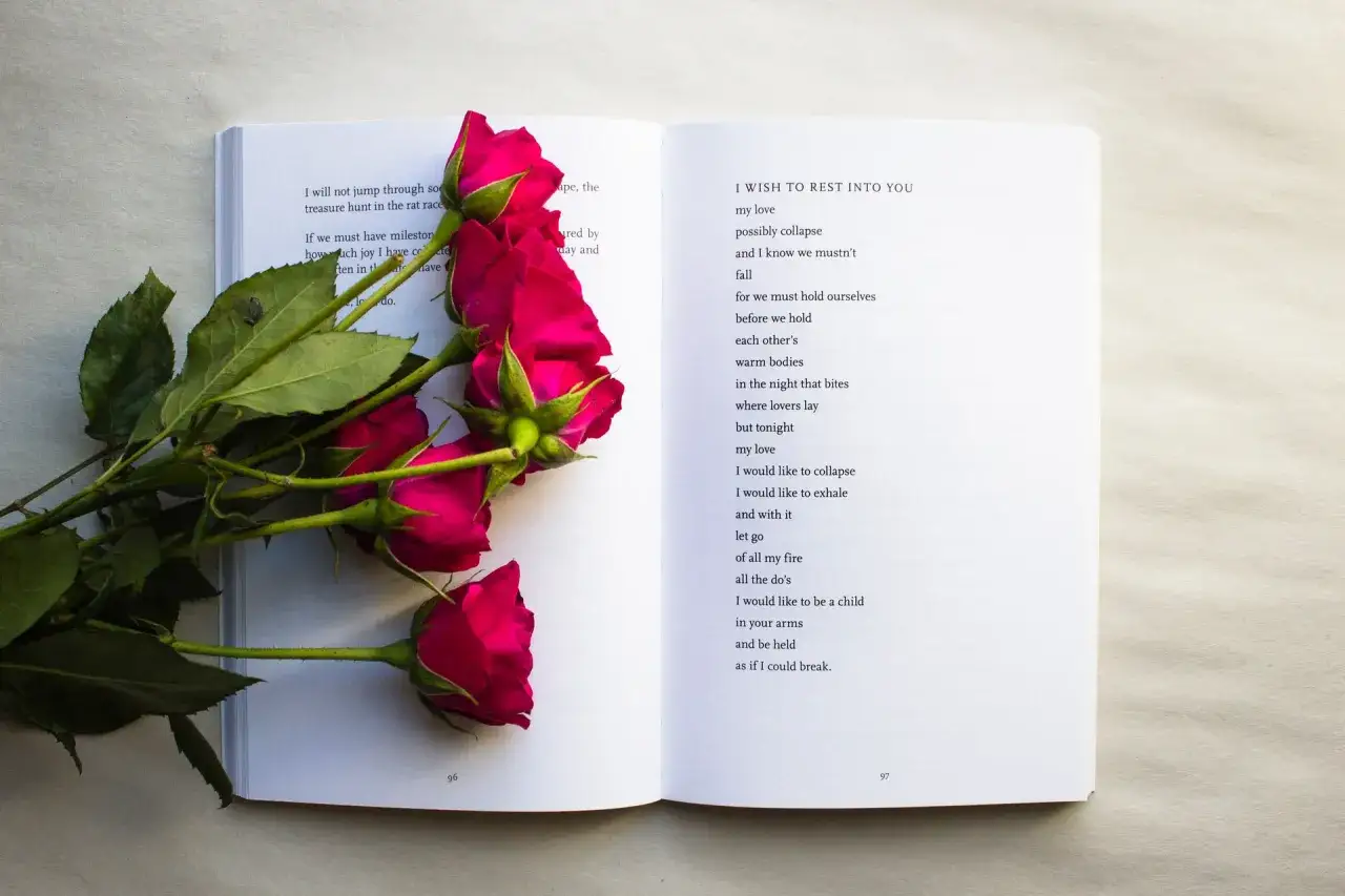 Czerwone róże na otwartej książce. Na lewej stronie wiersz, na prawej poezja 