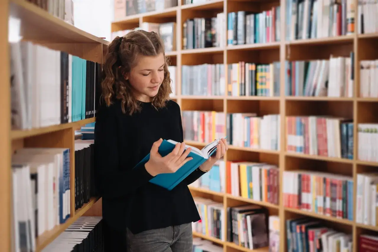 Dziewczynka w bibliotece, pochłonięta lekturą, odkrywa światy i odpowiedzi na pytanie, dlaczego warto czytać lektury.