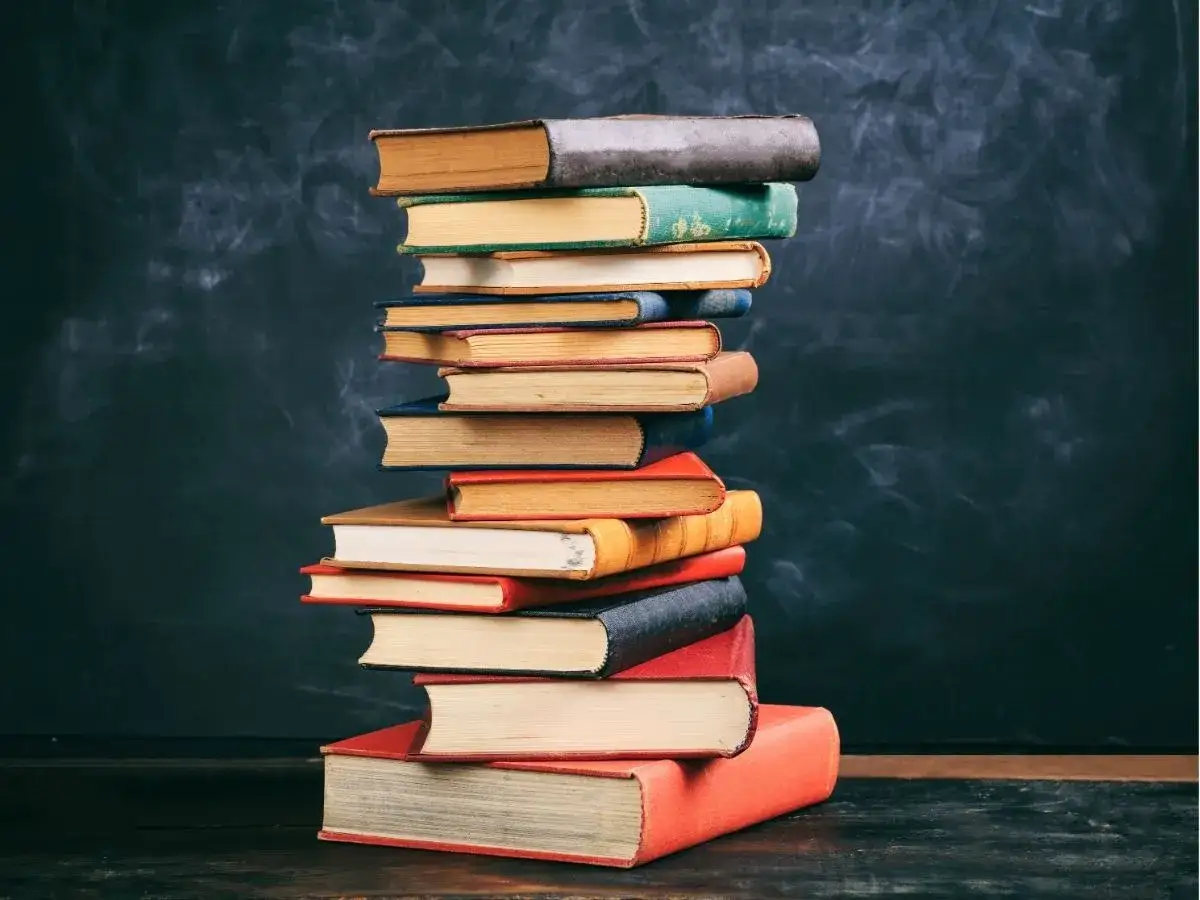 Stos książek na tle tablicy. Czy biblioteka przyjmuje książki? Może te stare, zakurzone egzemplarze znajdą nowe życie.