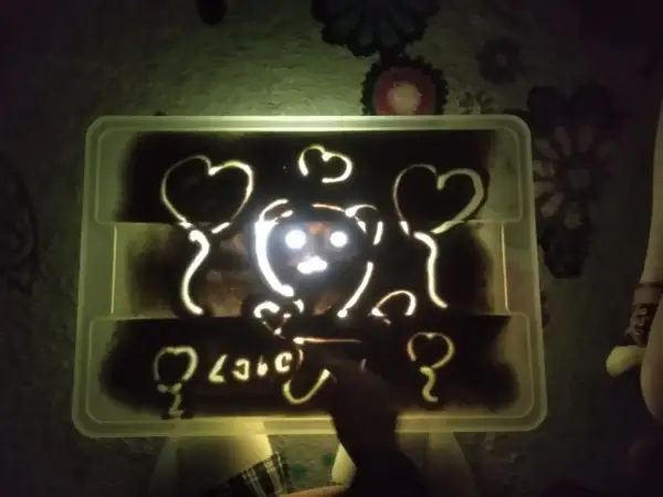 Napis "love" i misia z serduszkami na podświetlanej piaskownicy. Jak piękne smutne wiersze, które można wyczarować palcami.
