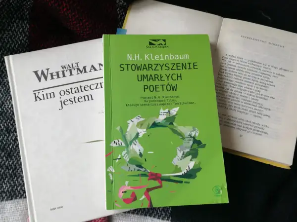 Zielona okładka "Stowarzyszenia Umarłych Poetów" N.H. Kleinbauma. Obok biała książka Walta Whitmana.