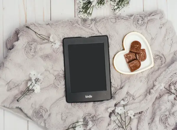 Elegancki Kindle na miękkim kocu z różami, obok serduszka z czekoladkami. Idealny zestaw, by dowiedzieć się, jak pobierać książki na Kindle.