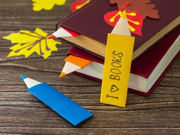 Jak zrobić ładną zakładkę do książki w kształcie kredki. Kolorowe zakładki wsuwają się między strony, a jedna z nich ma napis "I ♡ BOOKS".