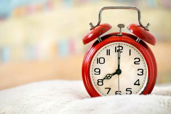 Czerwony budzik na białym tle, pokazuje 8:00. Czas na wierszyk na dzień dobry dla niego!